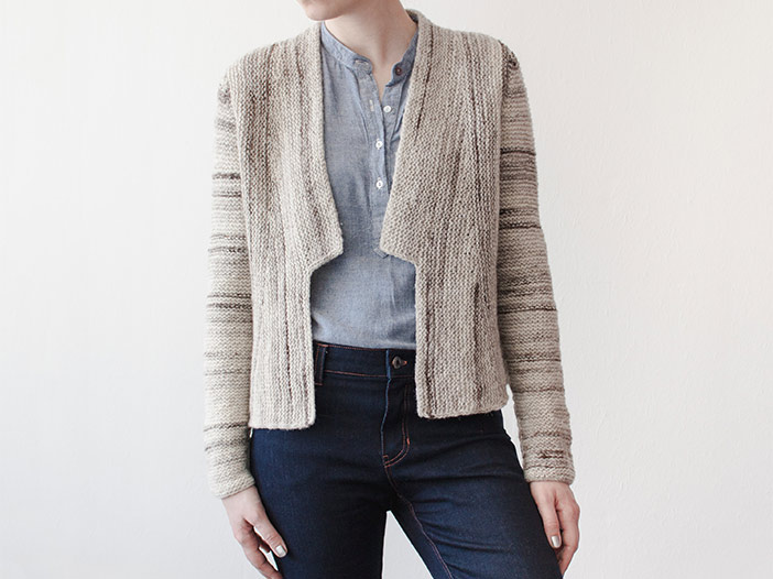 front view of woman wearing an open-front cardigan with lapels. Cardigan is worked in garter stitch in an off-white yarn streaked with dark brown, showing off the sideways construction of the body